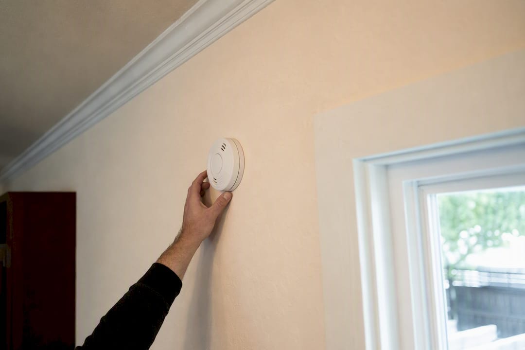 Hand adjusting wall-mounted smoke alarm installed too low