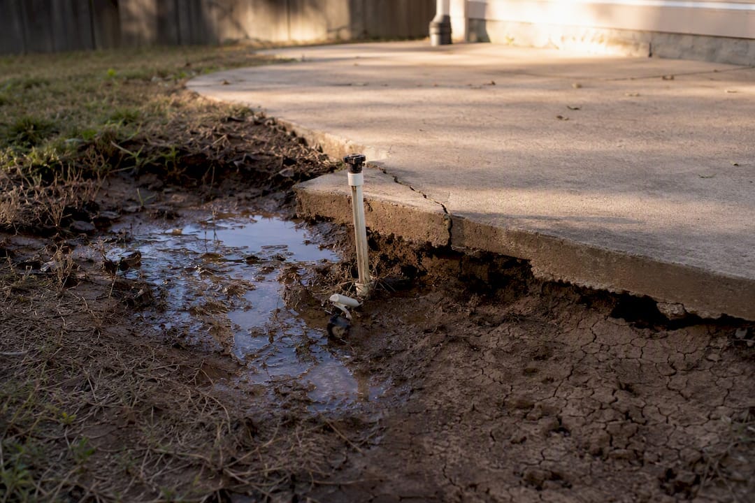 Broken sprinkler leaking onto clay soil near foundation